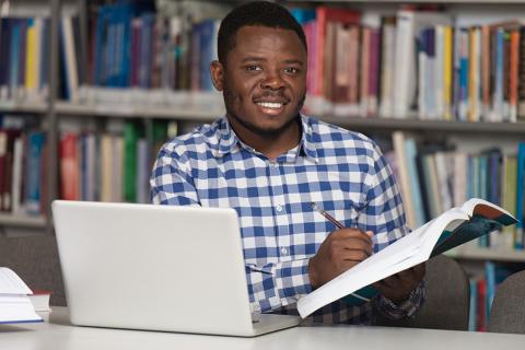 Black man writing in book sitting at laptop