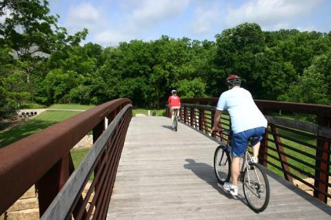Two people riding bikes over bridge on trail