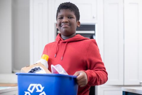 A young teen holds a recycling bin with various items that can be recycled curbside in Kanas City