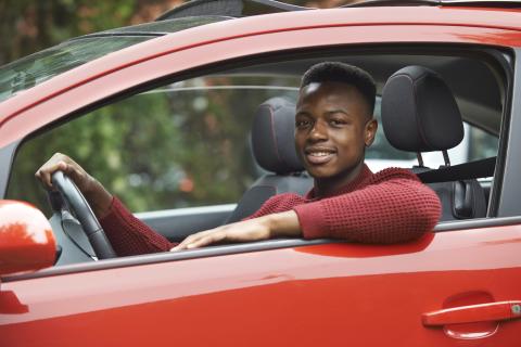 Black teenage boy in driver's seat of red car