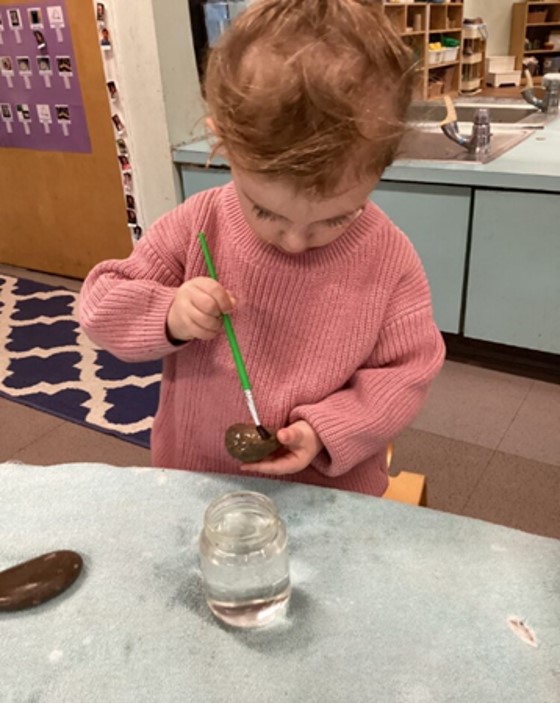 A child paints a rock in a preschool classroom