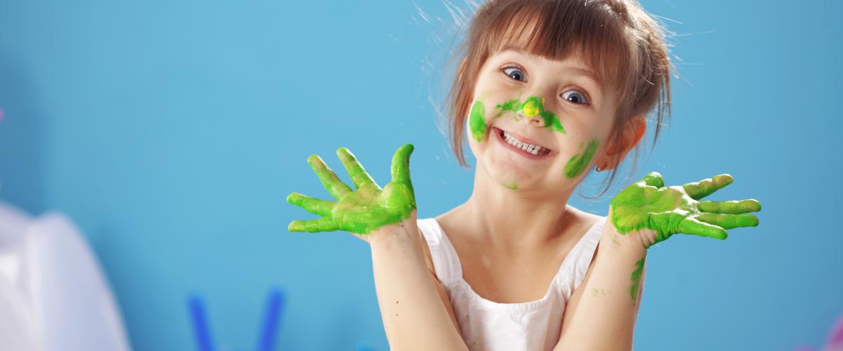 A young girl plays with green finger paint