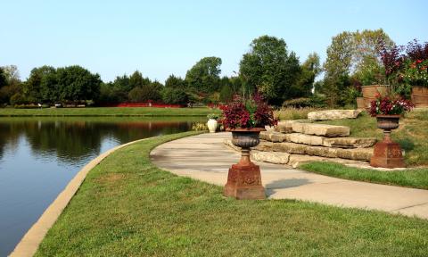 A sidewalk borders a pond at the Overland Park arboretum.