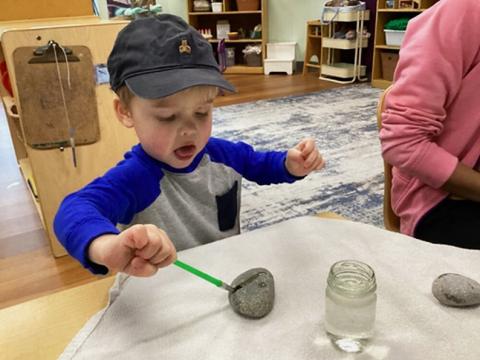 A child paints a rock in a preschool classroom