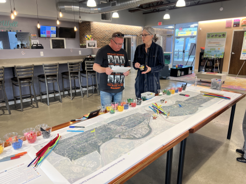 Two people talking with a long table with map of the corridor from Kansas City, Kansas to Independence, Missouri. 