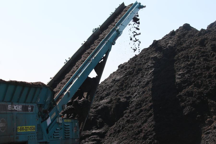 Belt loader piling organic material onto massive compost pile