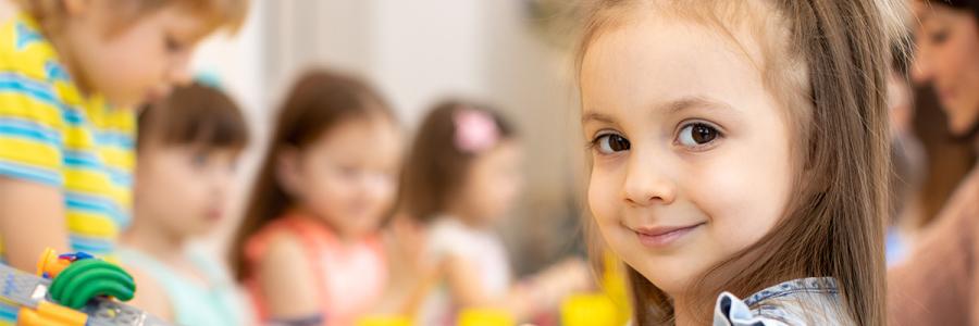 A girl in a preschool classroom looks at the camera