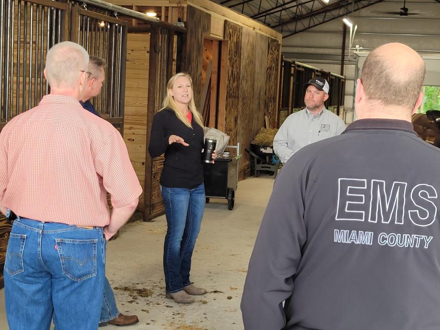 A person talking to a group of 911 commanders in a stable with therapy horses
